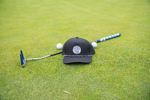 Black 19th Hole Rope Hat by Fore Over Par shown on a golf green with a putter and two balls behind it. 