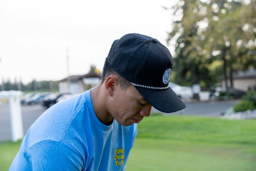 Man on a golf course wearing a black 19th Hole Rope Hat by Fore Over Par 