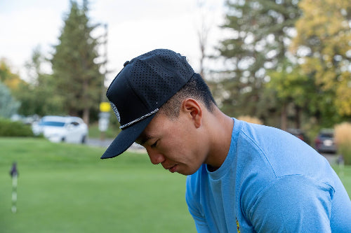 Man on a golf course wearing a black 19th Hole Rope Hat by Fore Over Par