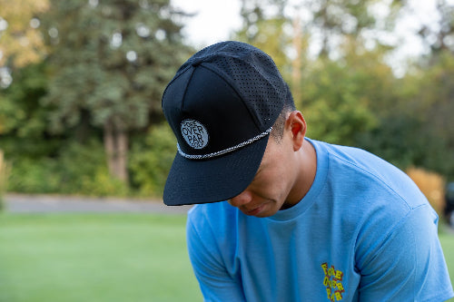 A man on a golf course wearing a black 19th Hole Rope Hat by Fore Over Par 