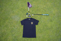 A black short-sleeve t-shirt with a alternative multicoloured Fore Over Par Logo, laid flat on a green grass background next to a purple flag, golf club, and golf balls.