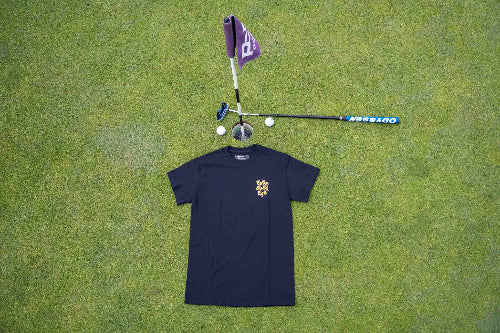 A black short-sleeve t-shirt with a alternative multicoloured Fore Over Par Logo, laid flat on a green grass background next to a purple flag, golf club, and golf balls.