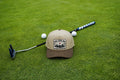 A beige and brown baseball cap with a 'Fore Over Par' graphic patch, styled on a green grass field with a golf putter, golf balls, and a golf club.