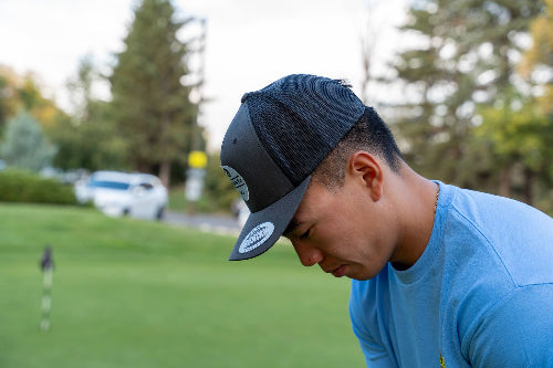 A man on a golf course wearing a charcoal and black OG hat by Fore Over Par