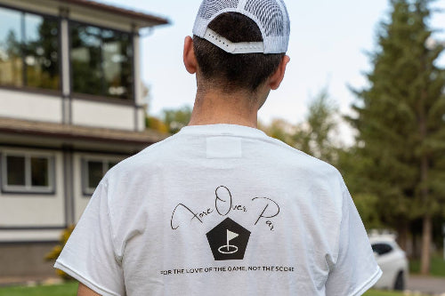 A 6'1" man viewed from behind wearing a large white t-shirt with a black graphic on the back that reads 'Fore Over Par' and 'For the love of the game', standing on a golf course.