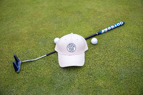 Cream Pony Tail Club Hat y Fore Over Par on a golf green with putter and golf balls behind it