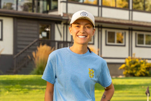 5'1" Female wearing a cream Pony Tail Club hat and Small light blue Fringe Society Tee Shirt by Fore over Par on Golf Course holding a putter