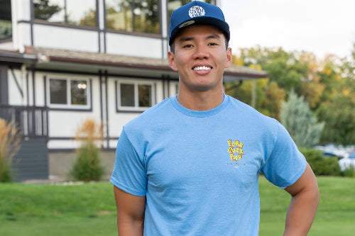 5'9" Male wearing dark blue 19th Hole Rope hat and a medium light blue Fringe Society tee shirt by Fore Over Par on golf course