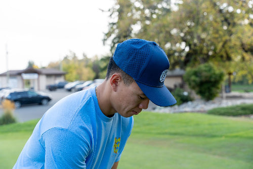 Male wearing a dark blue 19th Hole Rope hat by Fore oVer par on golf course. 