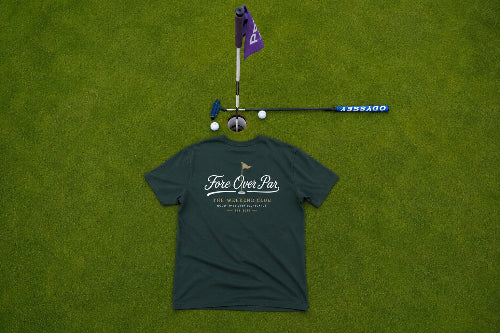 A green t-shirt laid flat on a green grass surface, with a golf putter and flagstick placed above it. The shirt has a white script logo reading 'Fore Over Par' and smaller text below.