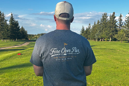 A 5'9" man viewed from behind wearing a grey t-shirt with 'Fore Over Par' printed on the back, standing on a green golf course under a blue sky.