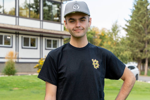 6'1" Man wearing a grey 19th Hole Rope hat and Large black Fringe Society Tee Shirt by Fore Over Par on a golf course. 