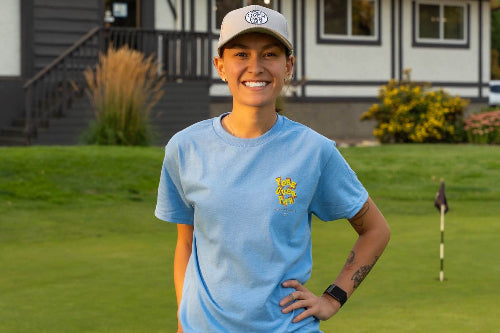 5'1" Woman wearing 19th Hole rope hat and a small light blue Fringe Society tee shirt by Fore Over Par standing on golf course.