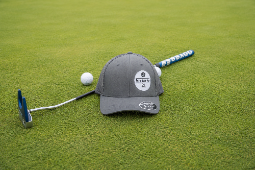 A grey Apex by Fore Over Par on a green with a putter and two golf balls behind it.