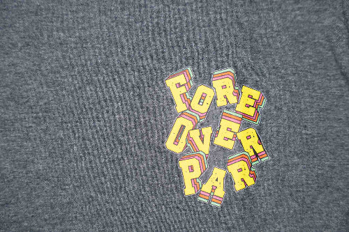 A close-up of a grey t-shirt featuring a colorful graphic print on the chest. The graphic displays the words 'FORE OVER PAR' stacked vertically in a bold, yellow 3D block font with red and orange striped accents and a light blue outline.