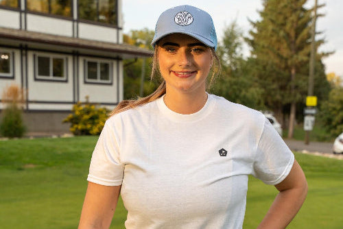 5'9" Female wearing a light blue 19th Hole Rope hat and large Clubhouse Tee by Fore Over Par on Golf Course. 