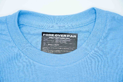 Close-up of a light blue crewneck t-shirt showing the inner neck label which reads 'FORE OVER PAR GOLF APPAREL, INC.' and 'SMALL PETIT.