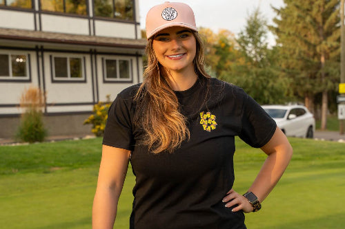 5'10" woman wearing a pink 19th Hole Rope hat and large black Fringe Society tee shirt by Fore Over Par on a golf course. 