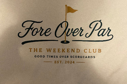A close-up of a sand-colored fabric surface printed with the text 'Fore Over Par' and 'The Weekend Club' in black and gold lettering, with a small golf flag graphic above the main text.