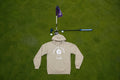 A sand pullover hoodie with a white 'Fore Over Par Golf' graphic is laid flat on a green grass surface, styled with a purple flag, golf club, and golf balls above it.