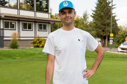 A 6'1" man on a golf course wearing a turquoise and white OG hat and large Clubhouse Tee by Fore Over Par